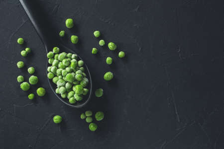 Frozen fresh farm green peas in plastic spoon on black background. Close-up. Top viewの写真素材