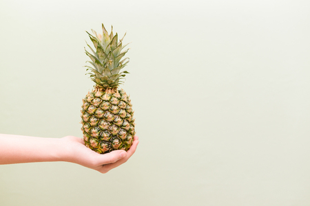 An outstretched female hand holds a ripe pineapple. The concept of sports, vegetarianism and healthy foodの写真素材