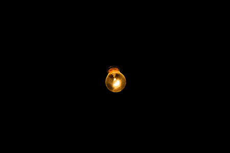 One glowing light bulb on a black background. Lamp shine warm, yellow light. Technology and inspirationの写真素材