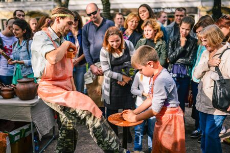 Russia, city Moscow - September 6, 2014: The child works on a potters wheel. A man teaches a boy to make a product out of clay. In the background viewersのeditorial素材