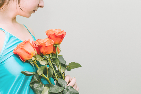 A young girl holds orange roses in her hands. A bouquet of bright flowers. On a beautiful girl wearing a turquoise shirtの写真素材