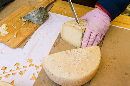 Closeup of hard cheese slicing. Worker on the market or in the shop slices cheese. Wooden board,...