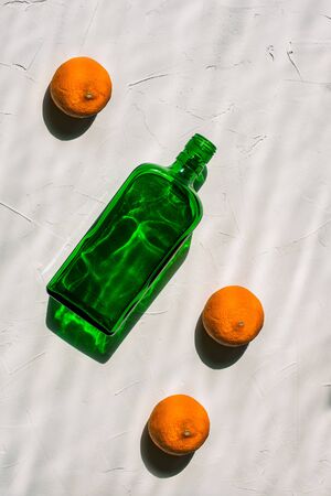 Green empty bottle and three mandarins on a white background. Minimal still life. Bright light, hard shadows and a reflection from the bottle. Creative style, art gallery. View from aboveの写真素材