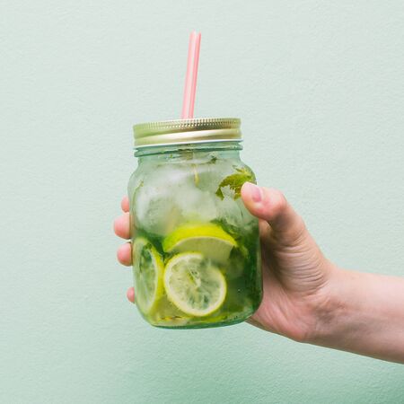 A girls hand is holding a jar of fruit drink. Non-alcoholic fresh cocktail in a glass goblet with a pink tube. Summer refreshing drinkの写真素材