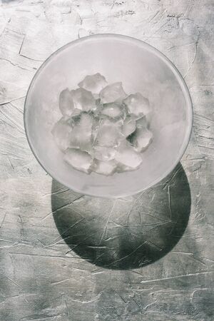 Glass plate with ice. Large ice cubes on a gray textural background. Hard shadow from the sun. Natural daylight from the window falls on a transparent plate. View from aboveの写真素材