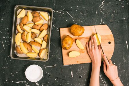 The girl cuts potato slices with a knife. Cooking fried potatoes. Peeled and chopped potatoes are laid in a baking tray. Chopping boardの写真素材