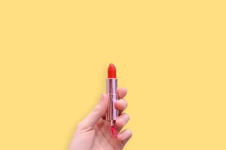 Red lipstick in a hand on a yellow background. Attributes of female cosmetics. Cosmetic product for applying makeup. Copy spaceの写真素材