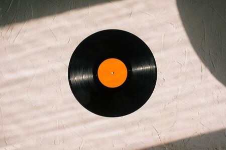 Vinyl record on a white background. Sunlight is falling on a black round disk and background. Retro...