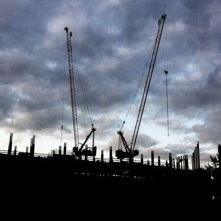 Silhouette of a crane at sunset. Construction cranes on a background of gray sky. Construction of a...
