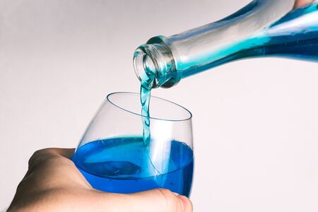 Pouring alcohol from a bottle into a glass goblet on a white background. Glass of wine and a bottle with pouring liquid. A stream of blue flows from the bottle.の写真素材