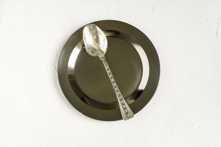 Round metal plate with a silver spoon. Antique cutlery with engraving on a white backgroundの写真素材