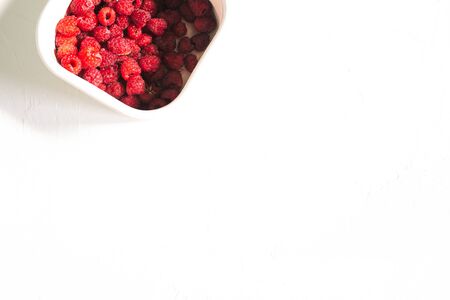 Colorful raspberry berries in white container. Fresh red raspberry berries on white background. Top...