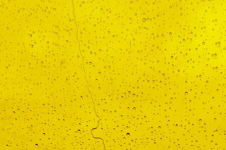 Raindrops on a yellow background. Flowing water from the surface of the windowの写真素材