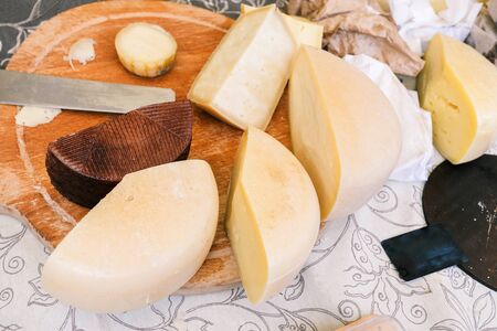 Different varieties of cheese on the table. Sliced pieces of cheese, knife and chopping wooden boardの写真素材
