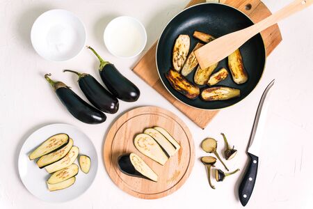 Fried eggplant on a white plate, top view. Sliced eggplant on a cutting wooden board with a knife, salt and butter. Cooking Fresh Vegetablesの写真素材