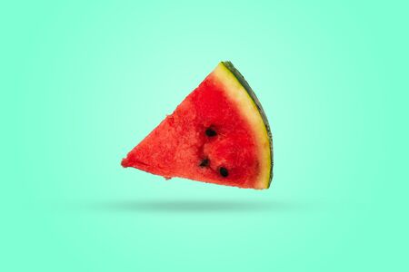 A piece of watermelon triangular in shape on a colored background. Ripe slice of fresh watermelon with red pulp and green peelの写真素材