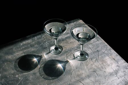 Glasses with martini on a dark background. Natural rays from the sun and shadow on a silvery texture. Minimalismの写真素材