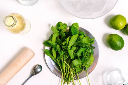 Cooking Mojito. Ingredients for a summer cocktail on the table. Mint leaves, lime and syrup. Ice in a glass plate and a metal spoonの写真素材