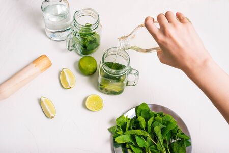 The barman pours syrup into a jar of ingredients for Mojito. Making an alcoholic cocktail. Fresh mint and lime on the tableの写真素材