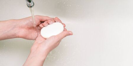 Girl holds soap in her hands. Hand washing in the sink with copy space. Coronavirus Prevention Antibacterial agent for cleaning hands of germs and bacteria. Infection prevention.の写真素材