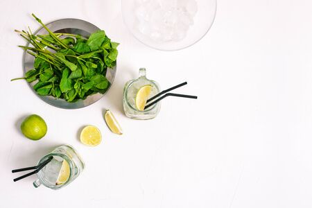 Glass goblets with an alcoholic drink Mojito. Ice, mint and slices of lime on a white table. Top view, copy spaceの写真素材