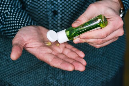 Man uses an antibacterial hand sanitizer. Plastic small bottle with green liquid. Hand antisepticの写真素材