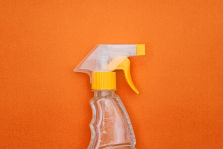 Spray with detergent on an orange background. Cleaning products in a clear plastic bottle. House cleaning and disinfection.の写真素材