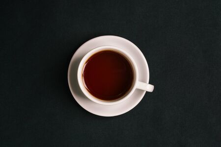 White cup with tea on a black background. Fragrant hot tea. Top view, flat layの写真素材