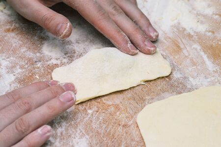 Women's hands make homemade pastries from the dough. Slice of puff pastry on a wooden board. Cooking foodの写真素材