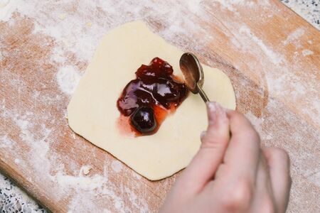 Cooking sweet buns. A female hand puts strawberry jam on the dough. Dough and jam on a wooden boardの写真素材
