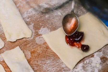 Making sweet homemade puff pastry. The cook puts strawberry jam on a piece of dough. Square slices...