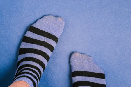 Men's legs in striped socks. Socks with black and blue stripes. A man is standing on colored paperの写真素材