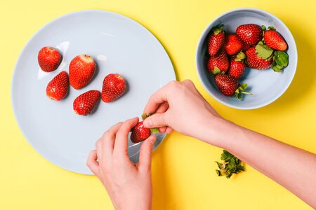 Man's hand holds strawberries on a yellow background. Blue plate with strawberries. Flat lay, top viewの写真素材