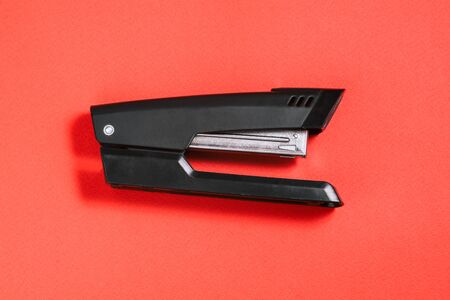 Large black office stapler on a red background. Stationery for stapling paper. Accessories for work