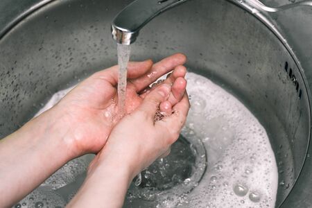 Hand washing under the tap with soap. A woman washes in the sink. Water flow, foam and spray. Hand treatment of dirt, germs and coronavirusの写真素材