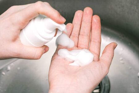 Putting whip foam soap bottle with foam on female hand. Lady using alcohol gel as hand sanitizerの写真素材