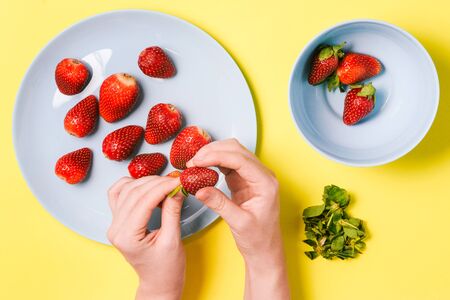 Girl peels strawberries for breakfast or to create cosmetics for face and hair. Woman's hand holds strawberries on a yellow backgroundの写真素材