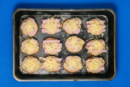 Sandwiches with sausage and cheese in a baking tray in the oven. The process of preparing a quick mealの写真素材