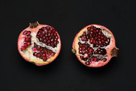 Two halves of a ripe pomegranate on a black background. Fresh red pomegranate with grains. The view from the topの写真素材