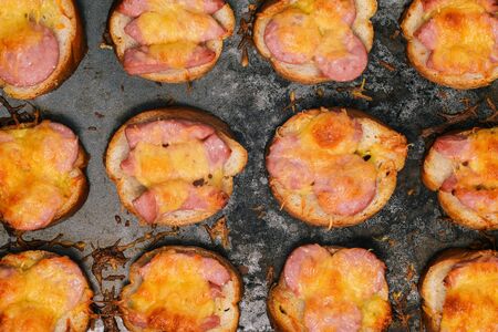 Melted cheese and fried sausages on bread. Baked sandwiches in a baking tray on a blue background. Close-up of food. Appetizer for Breakfast, lunch, dinner or beerの写真素材