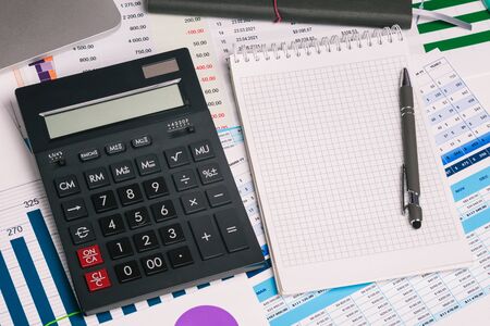 Calculator and an empty Notepad page on the office Desk with financial indicators and charts. Top view with a copy of the text input space. Finance and accounting. Company report.の写真素材