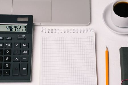 An office workplace with a calculator, laptop, coffee Cup, and Notepad with a blank page for text. A...