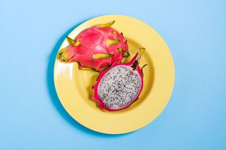 Cut dragon fruit in a yellow plate. Under pitaya with seeds on a colored background. Top view, flat layout.の写真素材