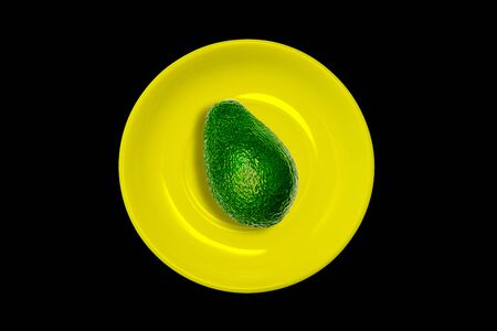 Yellow plate with avocado on a black background. Minimal colorful style.