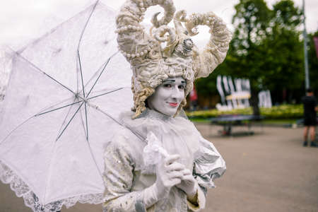Artist in a white suit and umbrella. On the head is an elegant and fashionable headdress with horns. On the face of white makeup. Russia, Moscow - September 10, 2016のeditorial素材