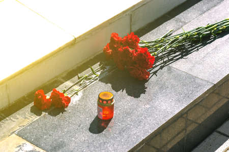 Red carnations on a marble slab. Flowers on the monument and a lamp. Symbol of mourningの写真素材