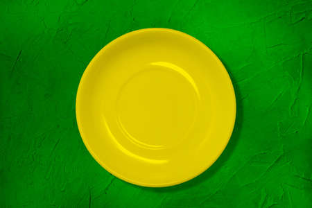 The plate on the table. Yellow empty plate on a green table with texture. The concept of cooking. Colored kitchen utensils. Minimal style. A top view of a flat layout.の写真素材