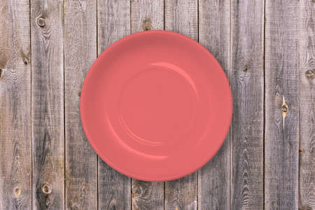 Plate on a wooden table. Red empty food plate. A dish for Breakfast, lunch and dinner. Tableware for home and restaurant. Concept of food and cooking. A top view of a flat layout.の写真素材