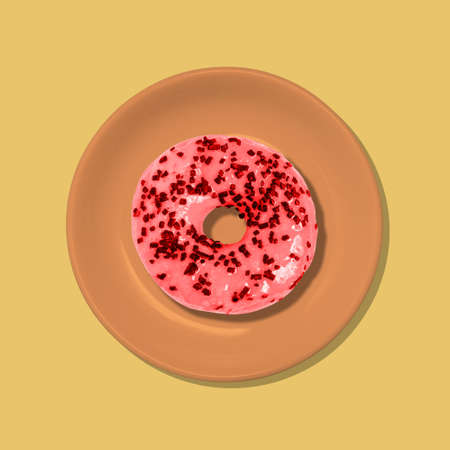 Red doughnut in an orange plate on a yellow background. Junk food. A top view of a flat layout. Minimal style.の写真素材
