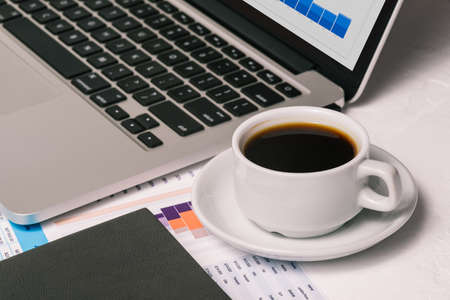 Laptop, a cup of coffee, and analytical charts. Desktop of a businessman. The concept of finance and investmentの写真素材